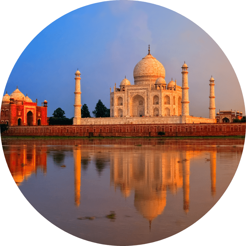 Le Taj Mahal au coucher du soleil, reflet doré dans les eaux du Yamuna, avec minarets et bâtiments adjacents.