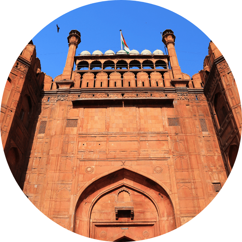Porte du Fort Rouge de Delhi, massive structure en grès rouge avec arche principale et minarets, drapeau indien flottant